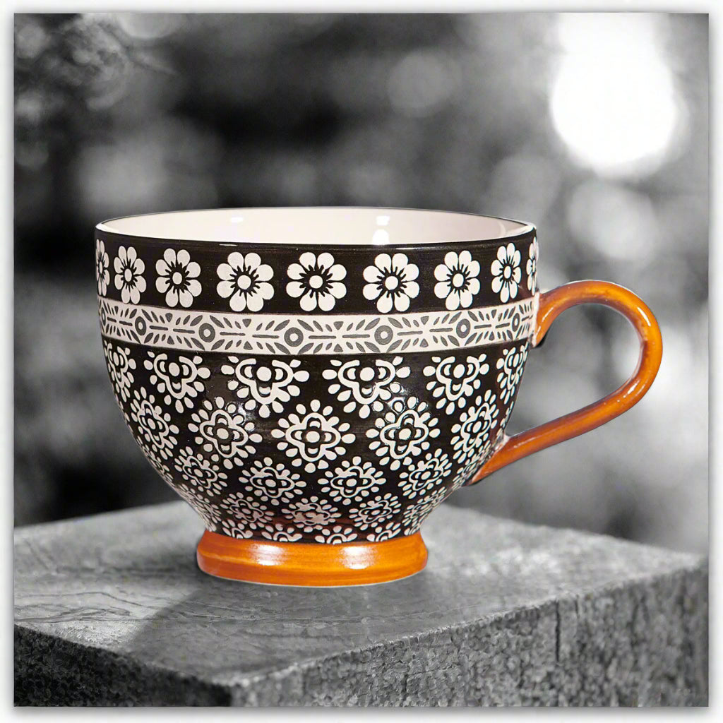 Ceramic mug with black floral pattern and orange handle on a white background